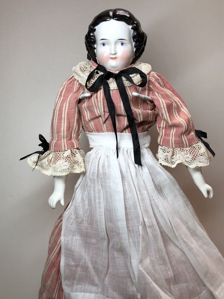 A brunette doll dressed in maid clothes and wearing a black head covering